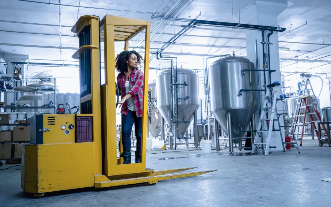 Mid adult woman in brewery driving forklift truck looking away