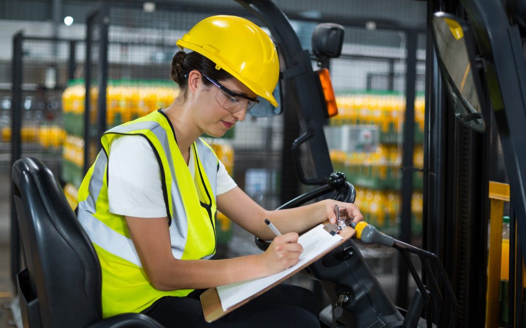 Female factory worker sitting on forklift and writing in clipboard at factory