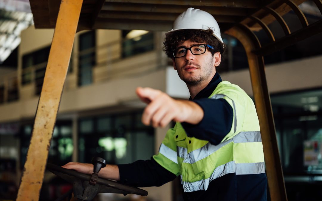 Male industrial engineer in white hard hat driving forklift