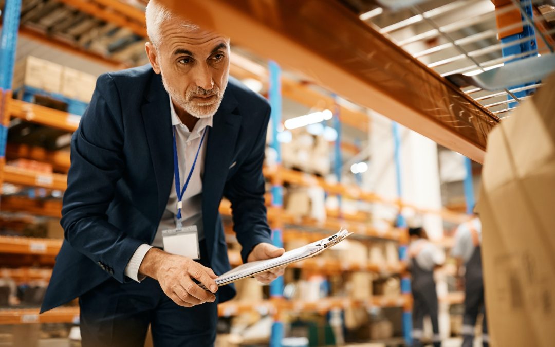 Mature warehouse manager checking stock of packages at storage compartment.