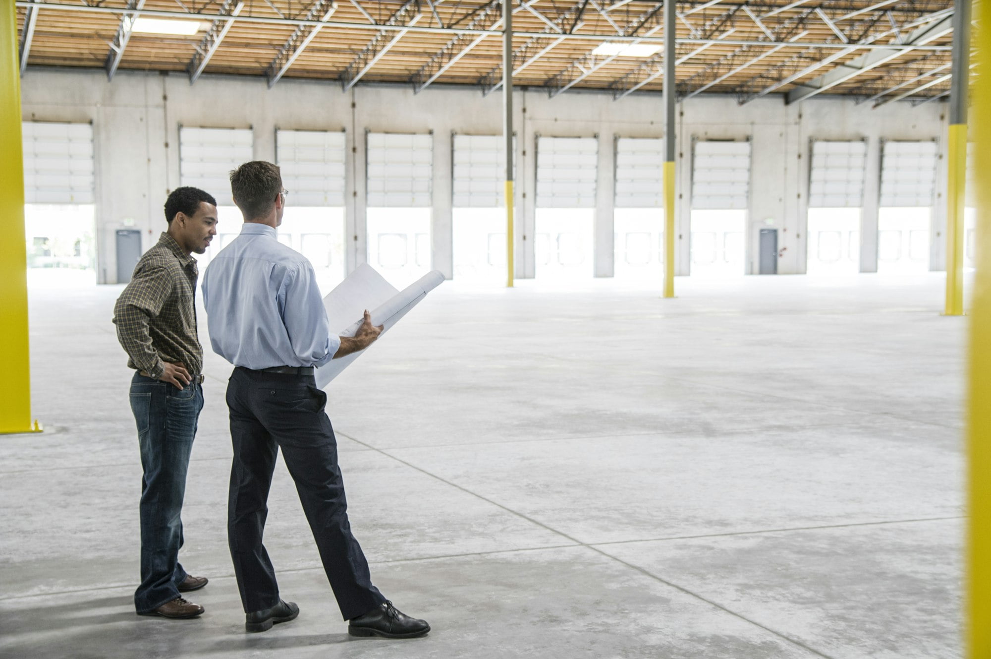 Back man owner of new warehouse and caucasian man architect going over blue print plans of new