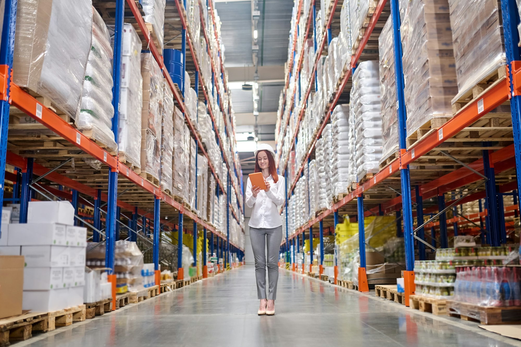 Elegant woman with tablet standing in warehouse aisle