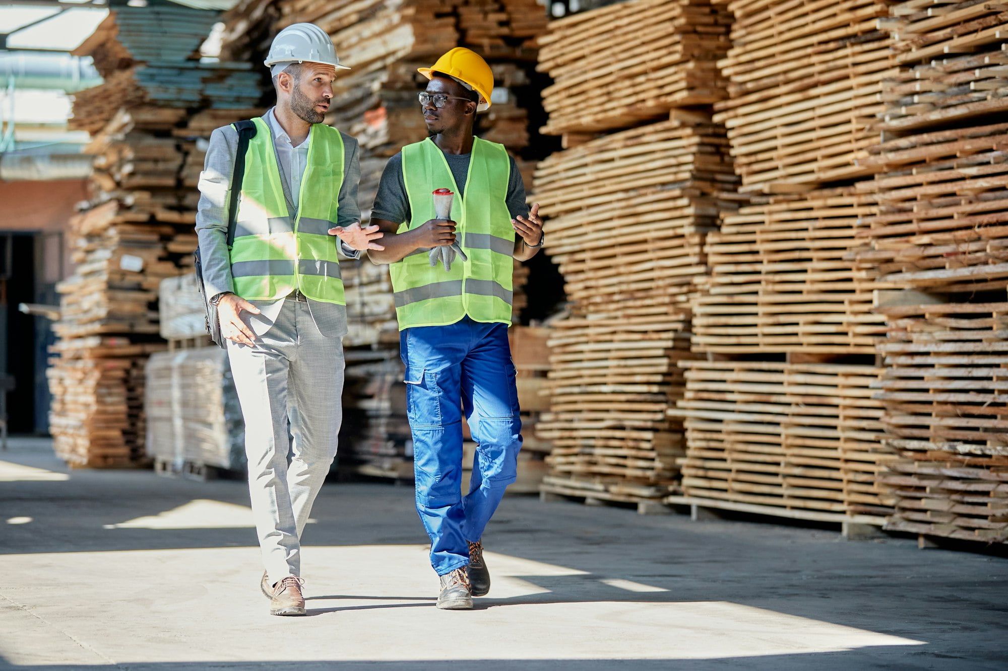 Warehouse manager talking to black worker while walking through lumber department.