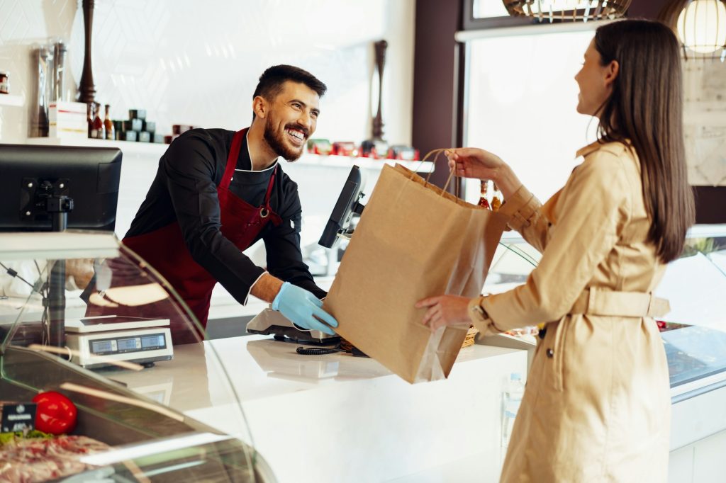 Shop assistant handling shopping bag to female customer in grocery store